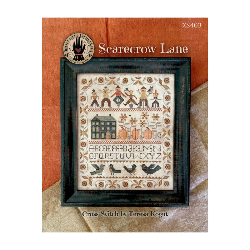 Front cover of the Scarecrow Lane cross stitch pattern finished in a black frame and laid on an orange and brown backdrop.