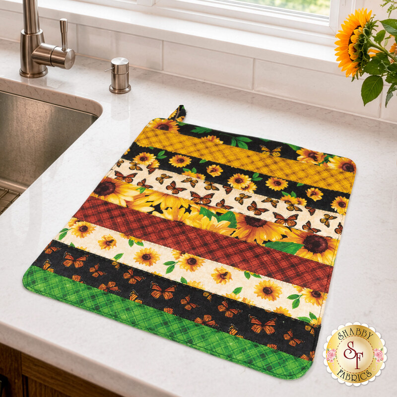 The completed Dry Ideas drying mat, colored in vibrant prints from the Sunshine Whispers collection by Wilmington Prints, staged on a marble kitchen counter with coordinating decor.