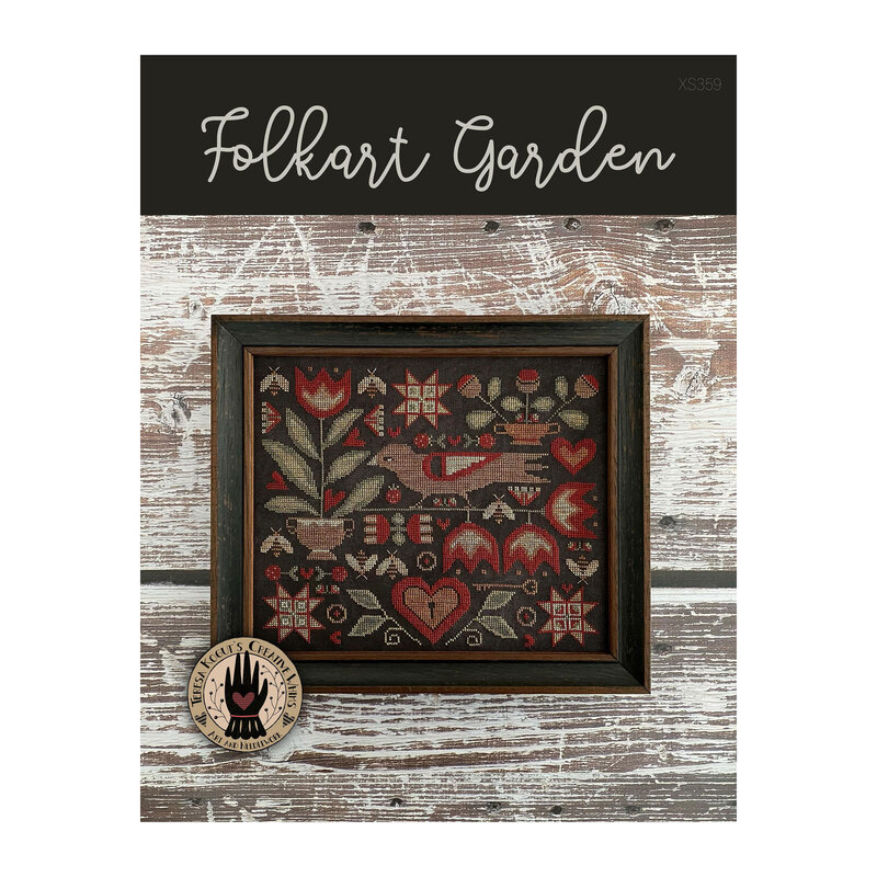 Front cover of the Folkart Garden cross stitch pattern finished in a rustic black frame hung on a wooden plank background.