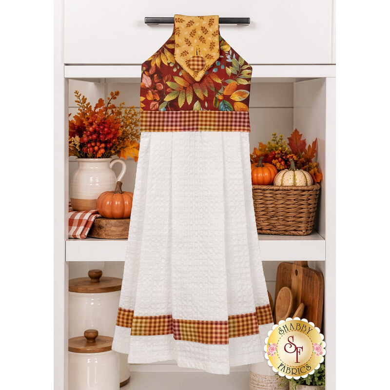 The completed Hanging Towel colored in warm autumnal fabrics from the Baskets of Autumn Blessings from Studio E Fabrics, staged on a kitchen drawer with coordinating décor.