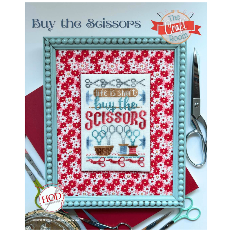 Image of the Buy The Scissors cross stitch project finished and framed, staged with scissors.