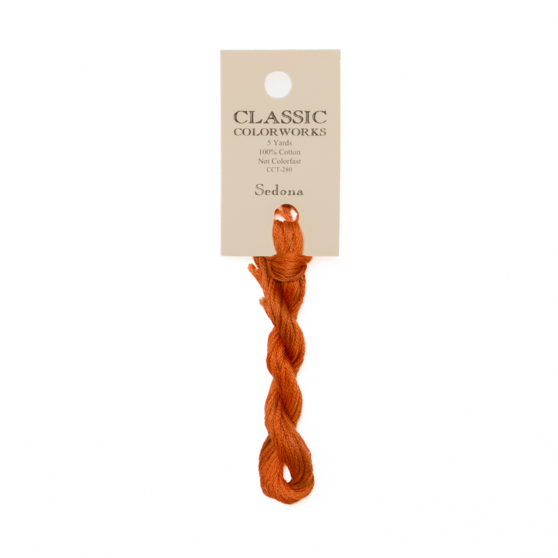 A skein of rusty orange-red embroidery floss, twisted and bundled, with a cream and black label featuring the brand name and color information.