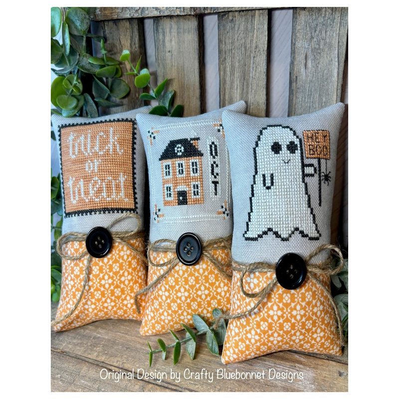 Image of the Halloween Smalls patterns completed as Halloween pillows staged on a wooden bench with greenery.