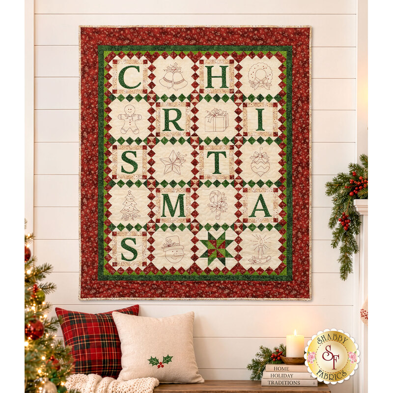 The completed C is for Christmas quilt, colored in red, green, and cream fabrics from the Christmastime collection by Maywood Studio, staged on a cream shiplap wall in a cozy living room filled with Christmas décor.