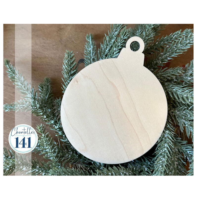 The unfinished round ornament, staged with a snow-frosted pine branch on a wood surface.