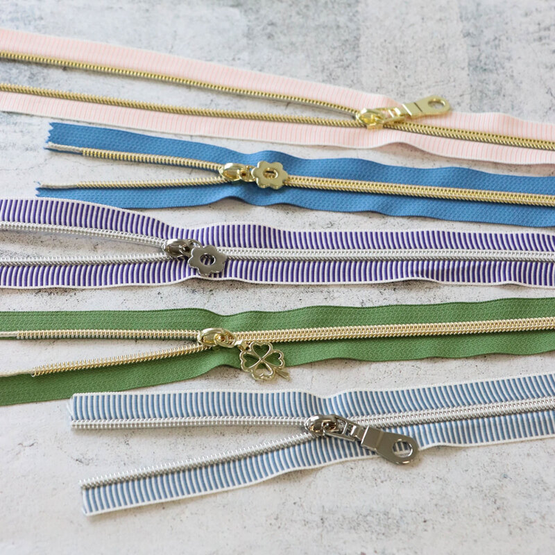 Five zipper pieces in various colors arranged horizontally, showing their coordinating novelty zipper pulls.