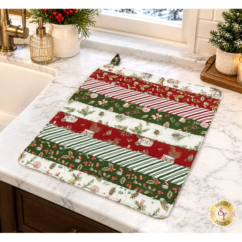 The completed Dry Ideas drying mat, colored in red, green, and white fabrics from the Holiday Spirit collection by Riley Blake Designs, staged on a white marble kitchen counter with coordinating decor.