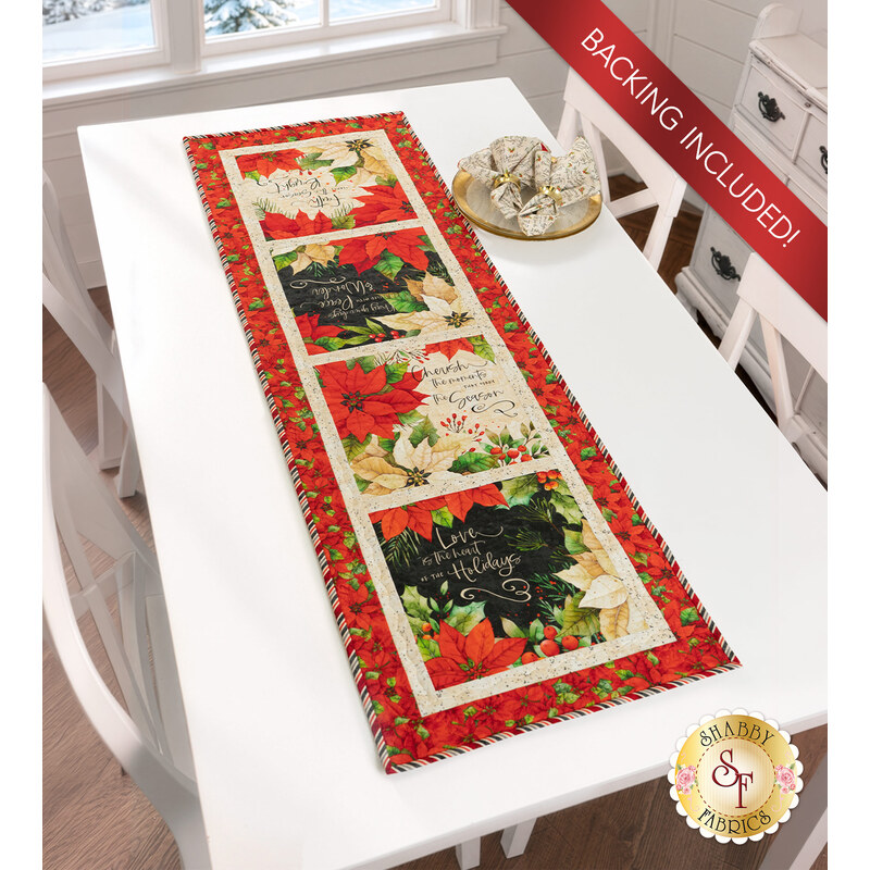 The completed Reason for the Season Table Runner, colored in red, cream, and black fabrics from the Poinsettia Radiance collection from White Owl Textiles, staged on a white table; a red banner in the upper right corner reads "Backing Included!"