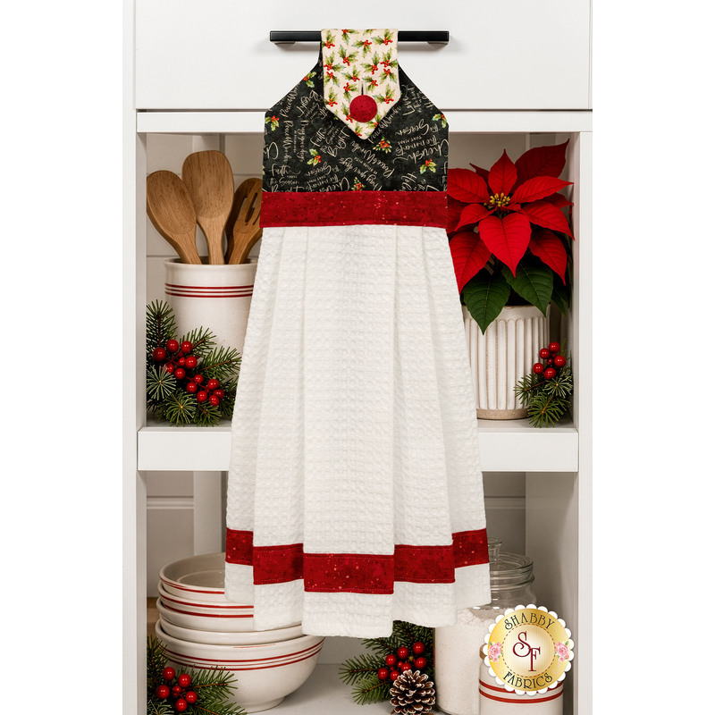The completed Hanging Towel colored in red, cream, and black fabrics from the Poinsettia Radiance collection from White Owl Textiles, staged on a kitchen drawer with coordinating decor.
