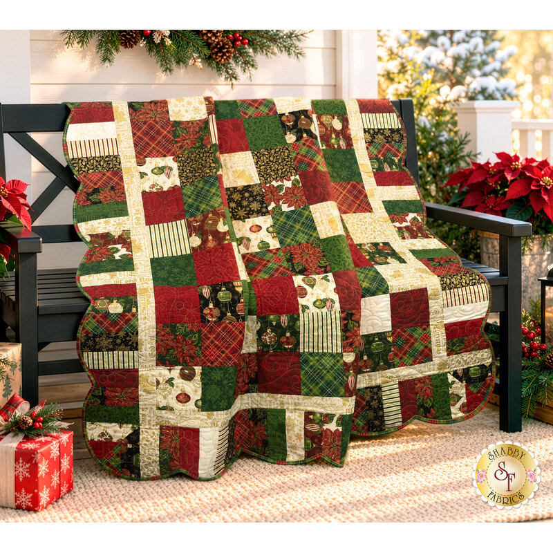The completed Holiday Charm Quilt, colored in red, green, cream, and gold metallic fabrics from the Poinsettias at Christmas collection by Jennifer Bosworth for Riley Blake Designs, artfully draped over a black bench on a porch and staged with coordinating flowers and décor.