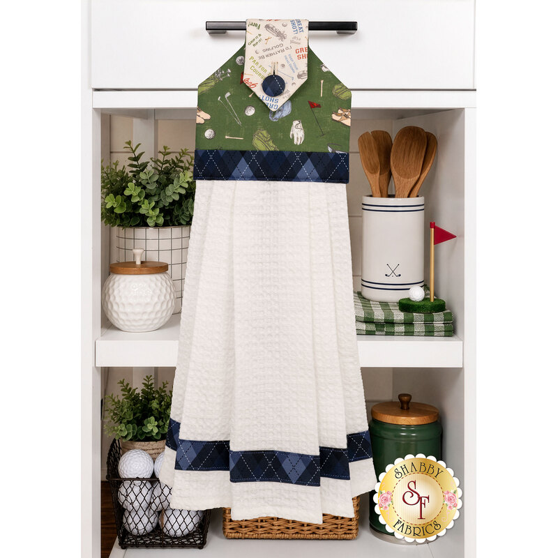 The completed Hanging Towel colored in green, navy, and cream fabrics from the Tee Time collection from Clothworks, staged on a kitchen drawer with coordinating decor.