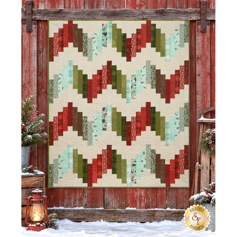 The completed Ridiculously Easy Jelly Roll Quilt colored in fabrics from the Snowtop Mountain Flannel collection by Maywood Studio, staged on a rustic red barn wall with coordinating décor.