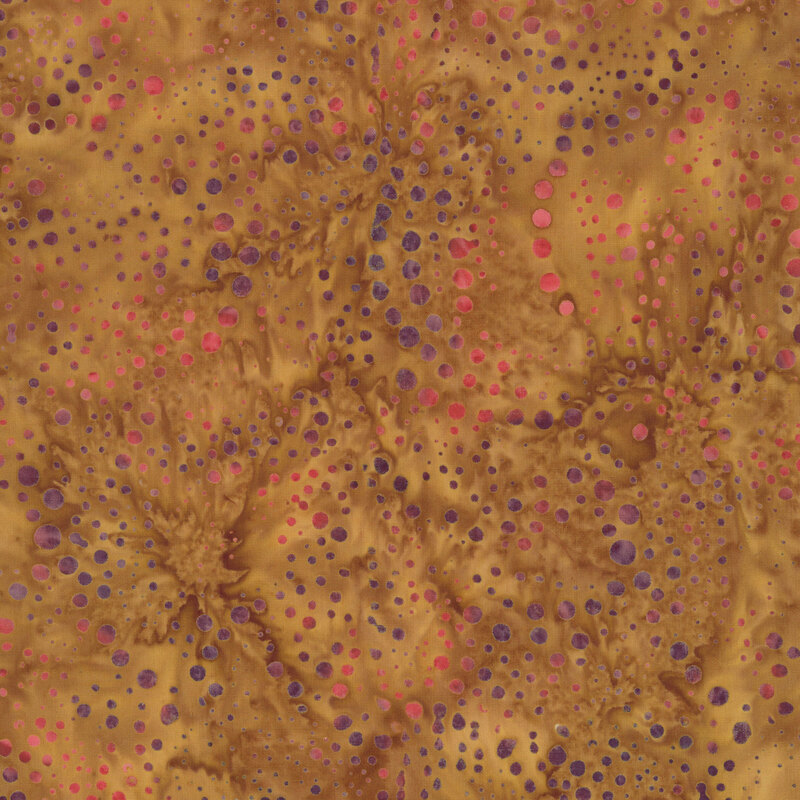 This warm, earthy batik fabric features scattered dots of varying sizes in shades of plum, mauve, and pink against a richly mottled golden brown background, creating a playful, textured look.