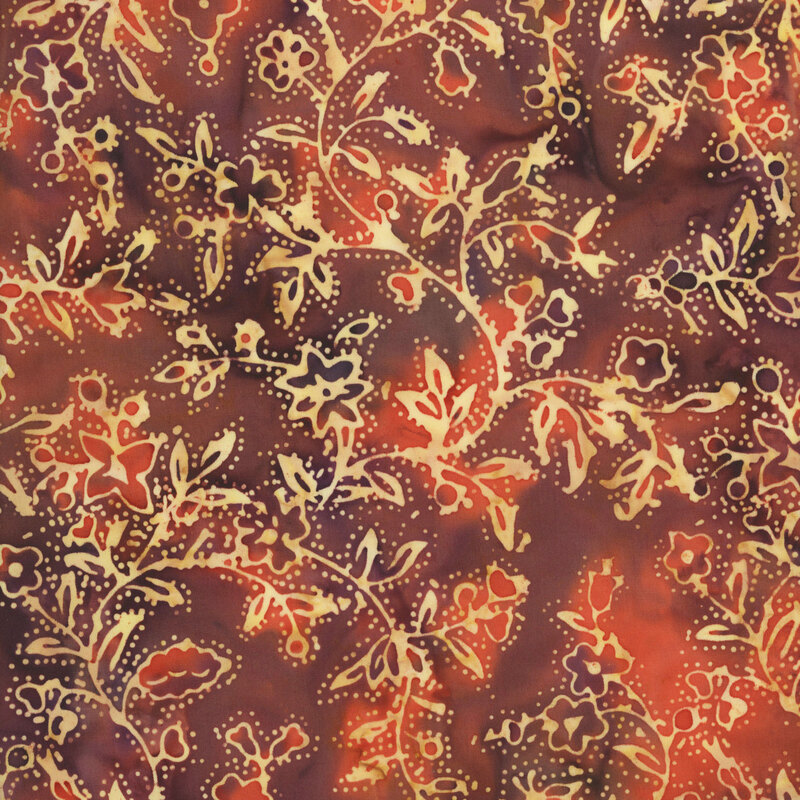 batik fabric featuring delicate, swirling floral vines, blossoms, and leafy motifs in warm shades of buff yellow against a richly mottled rust orange and burgundy-brown background.