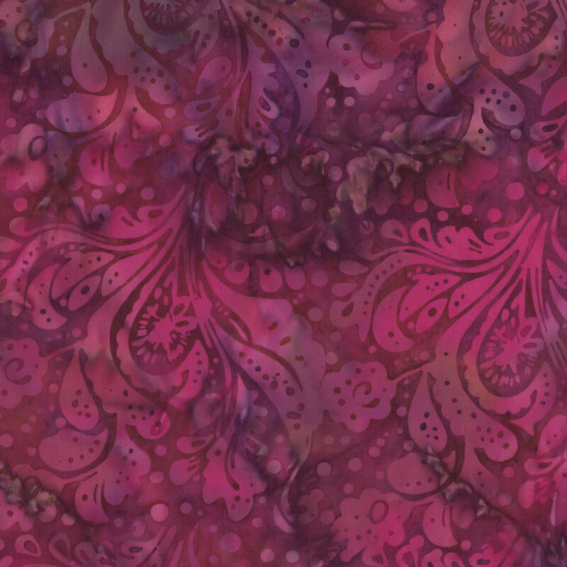 batik fabric featuring bold, swirling floral and paisley motifs accented with scattered dots in rich shades of magenta, raspberry pink, and deep plum against a softly mottled background.