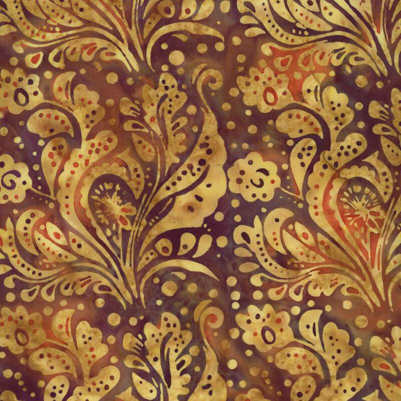 batik fabric featuring paisley-inspired florals, graceful leaves, and scattered dots in warm shades of golden yellow, against a deep burgundy and rust mottled background.