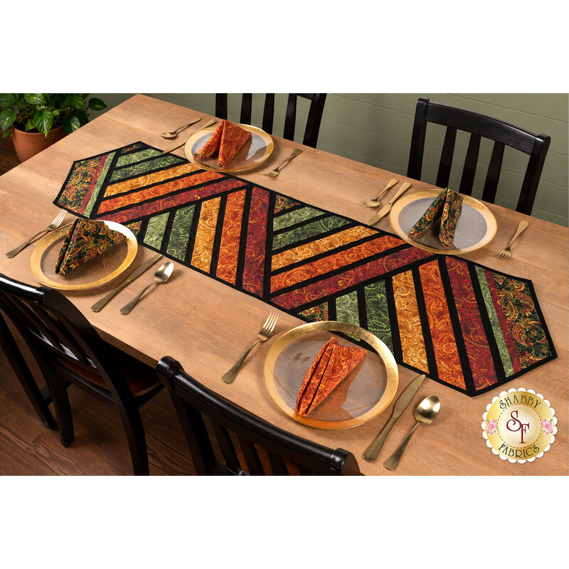 The completed Greased Lightning Table Runner colored in warm fall fabrics from the Harvest Beauty collection by Benartex, staged on a warm wooden table with four coordinating napkins and table settings.