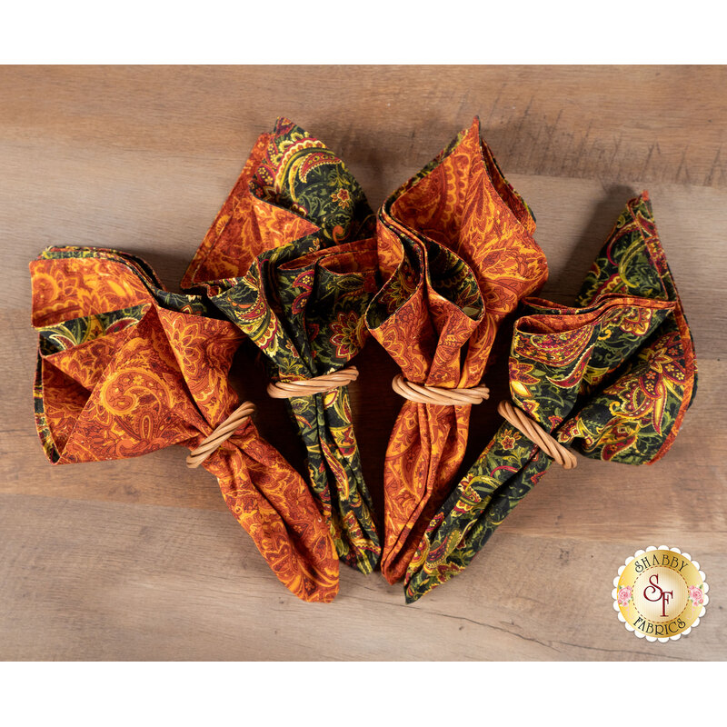 A top down shot of the napkins, colored in warm fall fabrics from the Harvest Beauty collection by Benartex, staged on a warm wooden table.