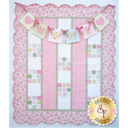 A quilt with a floral border featuring alternating pink and white blocks arranged in vertical stripes. Above the quilt, there is a banner spelling HOPE with pastel-colored letters and decorative hearts. A logo from Shabby Fabrics is located at the bottom right corner.