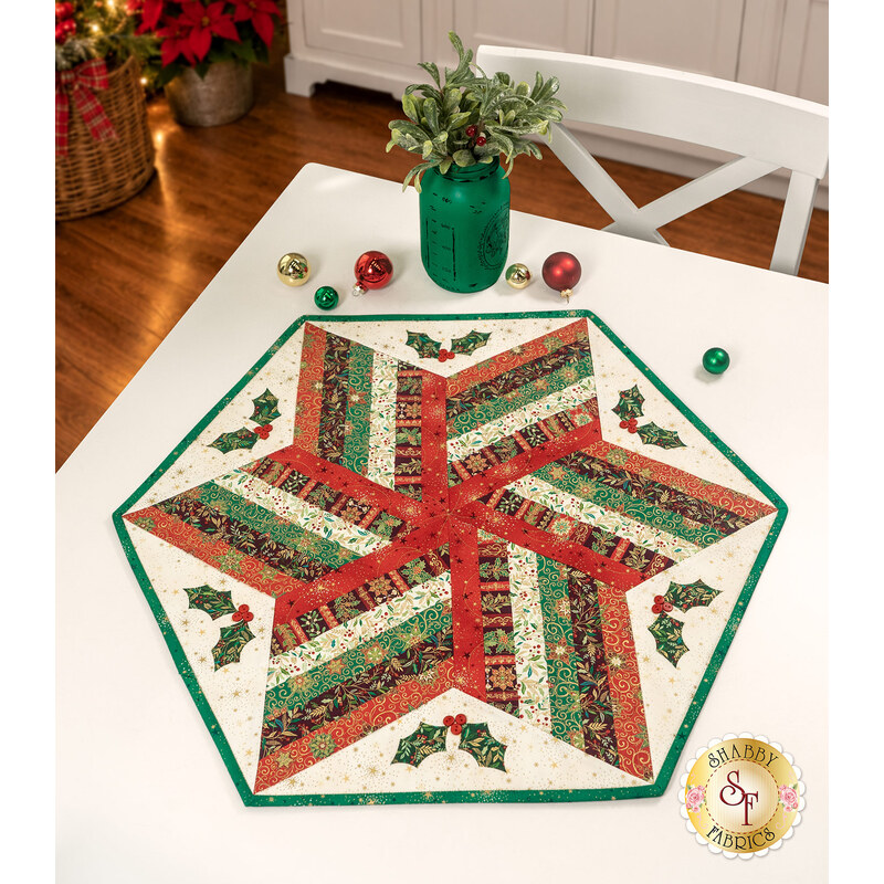 The completed 60 Degree Diamond Table Topper colored in cream, red, and green fabrics with gold metallic accents from the Adorn collection by Andover Fabrics, staged on a white table with coordinating décor.