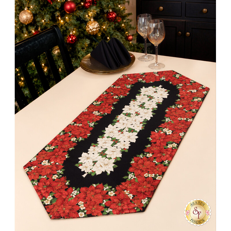 The completed Easy Striped Table Runner, colored in black, red, and cream fabrics with gold metallic accents from the Merry Christmas 2026 collection by Timeless Treasures, staged on a cream table with coordinating glasses and décor.