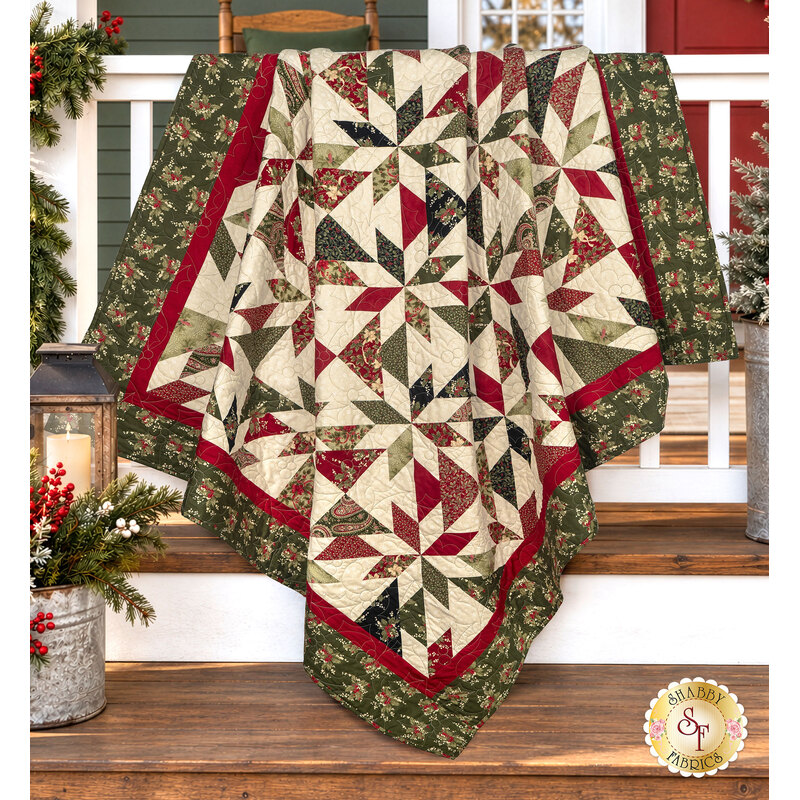 The completed Playing Favorites Quilt, colored in rich cream, red, and sage and forest green fabrics from the Candlelight Christmas collection by Moda Fabrics, artfully draped over a white porch railing and staged with understated, coordinating décor.