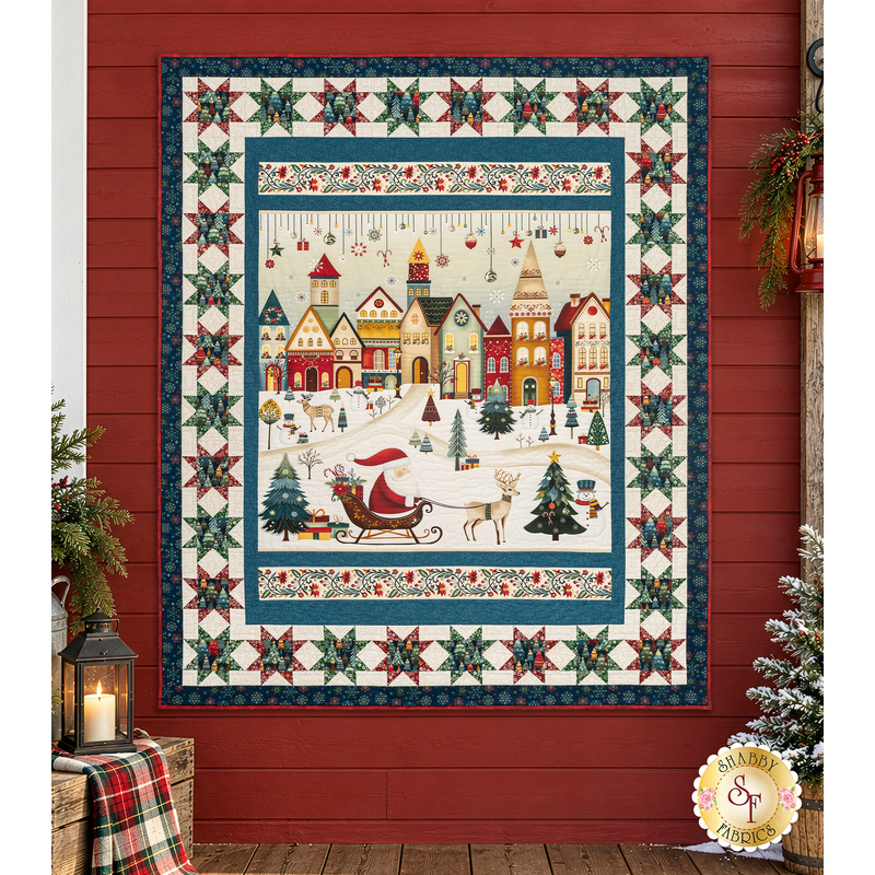 The completed Starry Night Panel Quilt, colored in unique fabrics from the Nordic Holiday Village collection by Henry Glass Fabrics, hung on a red barn wall and staged with coordinating décor.
