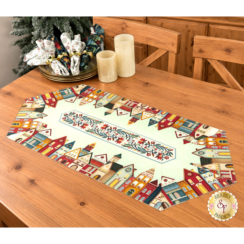 The completed Easy Striped Table Runner colored in mint, red, yellow, cream, and teal blue fabrics from the Nordic Holiday Village collection by Henry Glass Fabrics, staged on a Nordic spruce table with coordinating décor, napkins, and table settings.