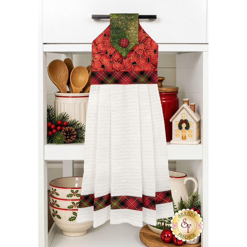 The completed Hanging Towel Kit colored in black, red, and cream fabrics with gold metallic accents from the Merry Christmas 2026 collection by Timeless Treasures, hung on a drawer surrounded by coordinating décor.