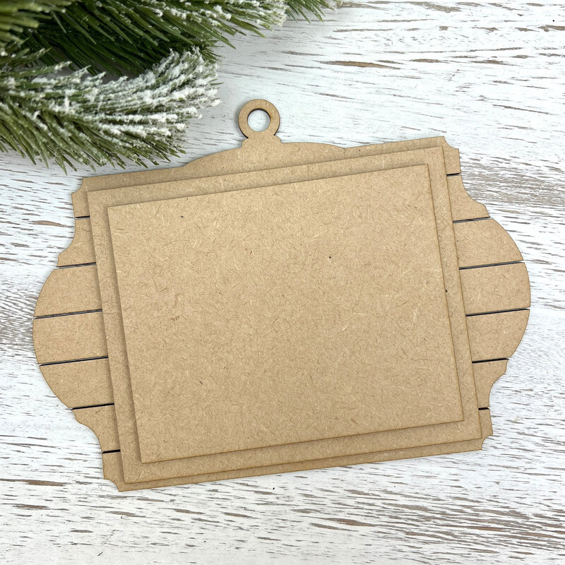 Unfinished layered MDF ornament display with a shiplap-style frame, hanging loop, and rectangular mounting boards for holding a small stitched piece.