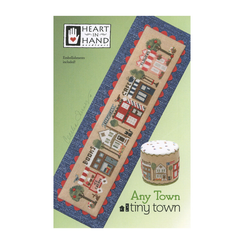 Front cover of the Any Town Tiny Town cross stitch pattern with the finished design on a denim fabric isolated on a green background.