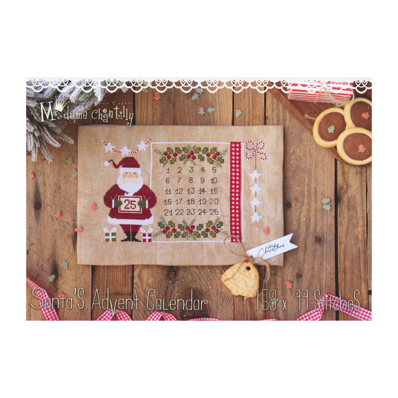 Front cover of the Santa's Advent Calendar cross stitch pattern showing the finished pattern laid on a wooden plank table next to ribbon, shortbread cookies, and a pine bough.