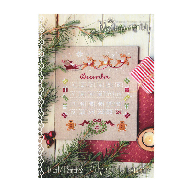 Front cover of the Santa's Advent Calendar cross stitch pattern showing the finished pattern laid on a wooden plank table next to a candle, a striped box, and pine boughs.