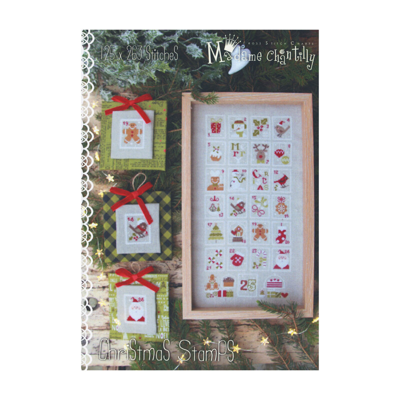 Front cover of the Christmas Stamps cross stitch pattern showing the finished pattern laid on a wooden plank table on top of pine boughs, holy sprigs, and Christmas lights next to the alternative stamp designs.