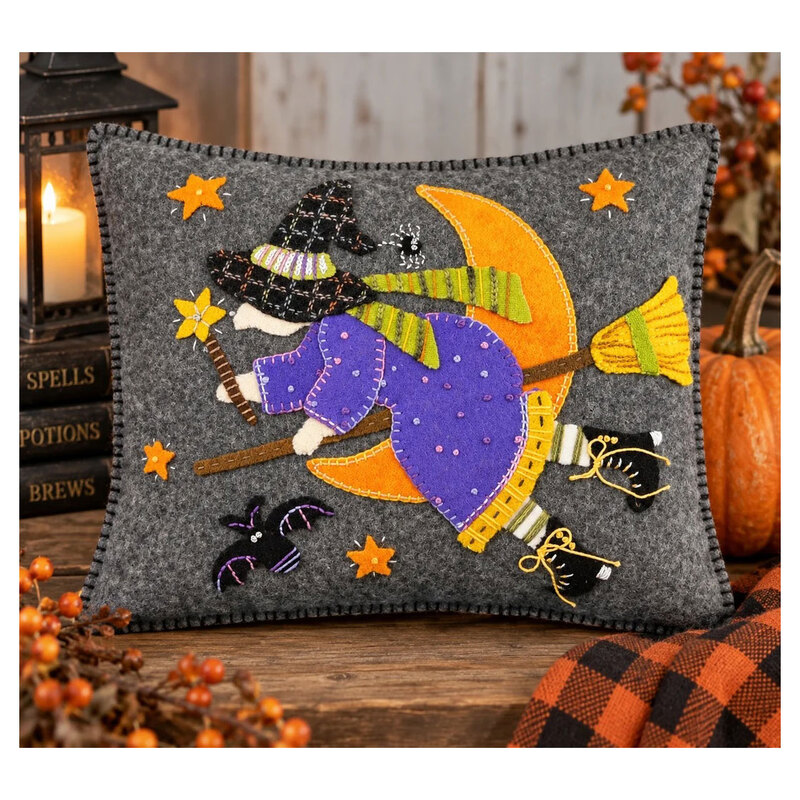 The finished Hilde and Friends pillow featuring a witch flying on a broom across a charcoal sky with a crescent moon and stars accompanied by a bat and spider