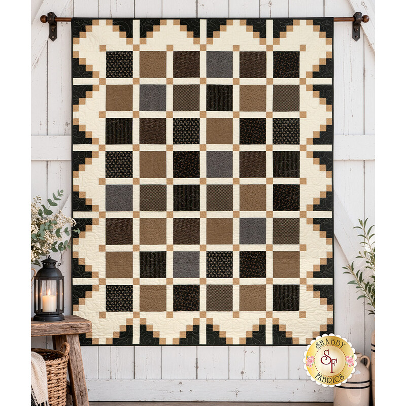 The completed Simply Cool Quilt, colored in cozy neutrals from the Black Sheep Cottons collections by Marcus Fabrics, hung on a white barn door wall and staged with coordinating décor.