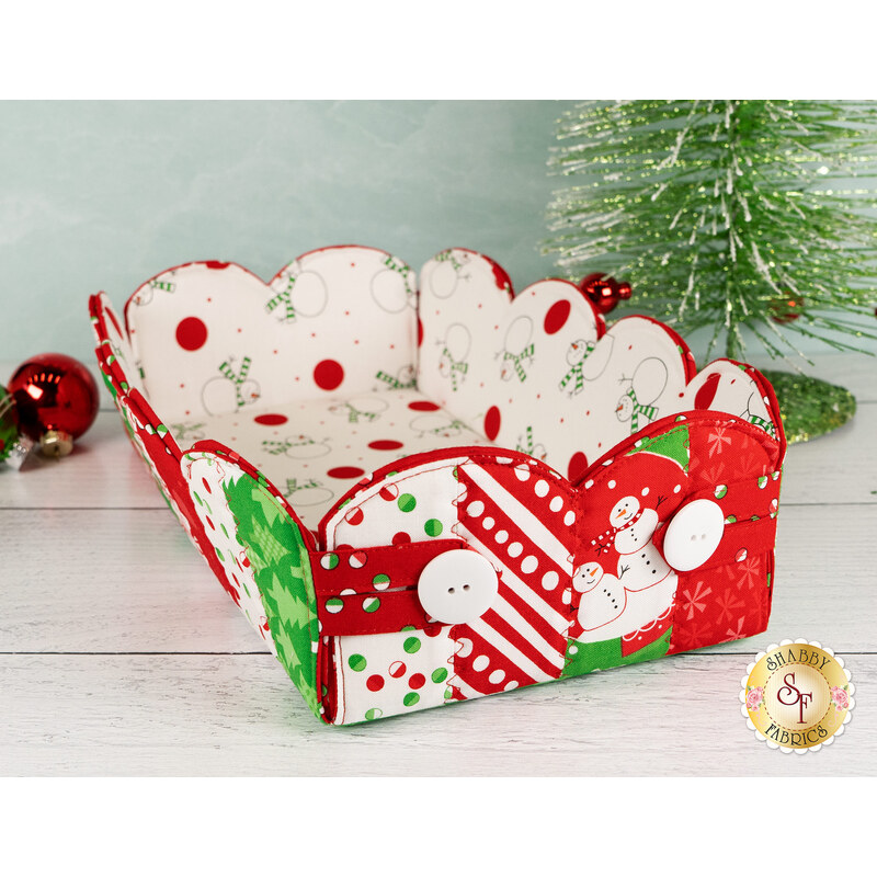 The completed Scalloped Basket, colored in bright red, green, and white fabrics from the Snow Time collection by Moda Fabrics, staged on a white wood table with coordinating décor.