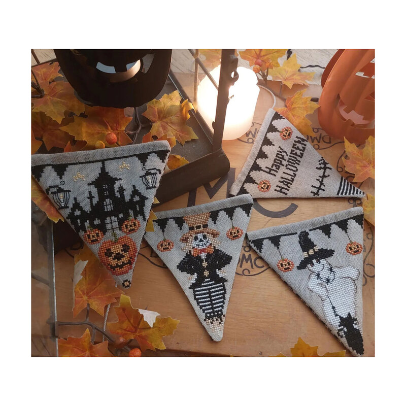 Photo of the four finished Happy Halloween Flag patterns laid out next to jack-o'-lanterns, fall leaves, branches, candles, and a lantern.