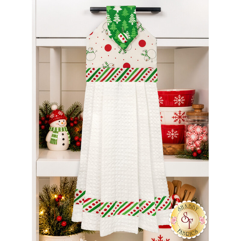 A head on shot of the completed Hanging Towel, colored in bright red, green, and white fabrics from the Snow Time collection by Moda Fabrics, hung on kitchen drawer and staged with coordinating décor.