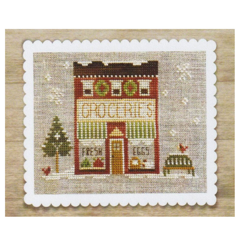 Cross-stitch of a small grocery shop with a tree, an eggs sign, and a scalloped white border.