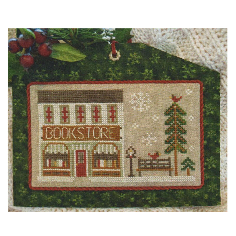Cross-stitched bookstore scene with a building, tree, bench, and snowflakes.