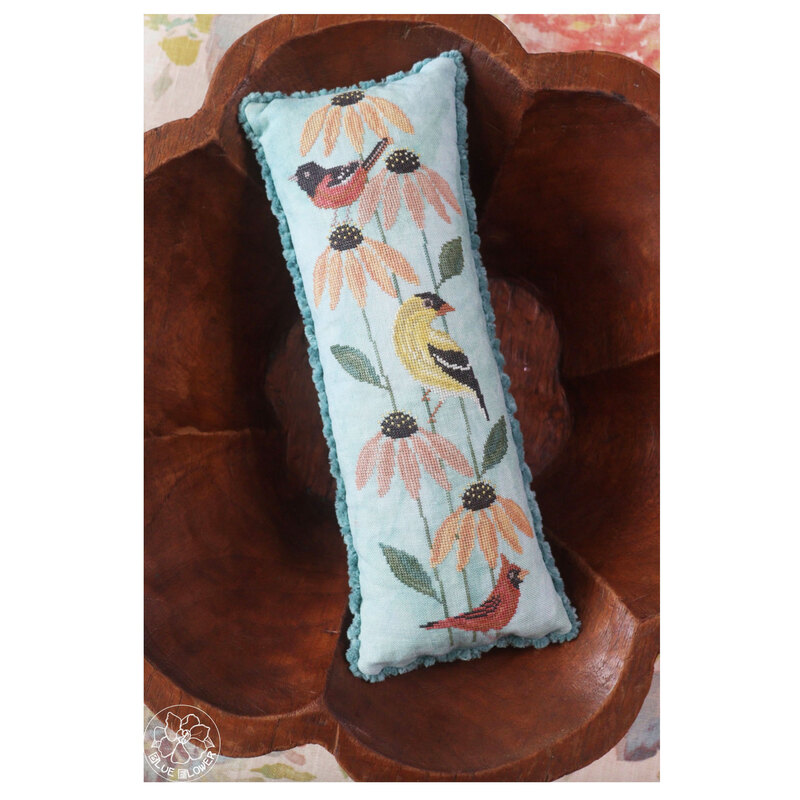 The finished pillow with three birds resting inside a wooden bowl. 