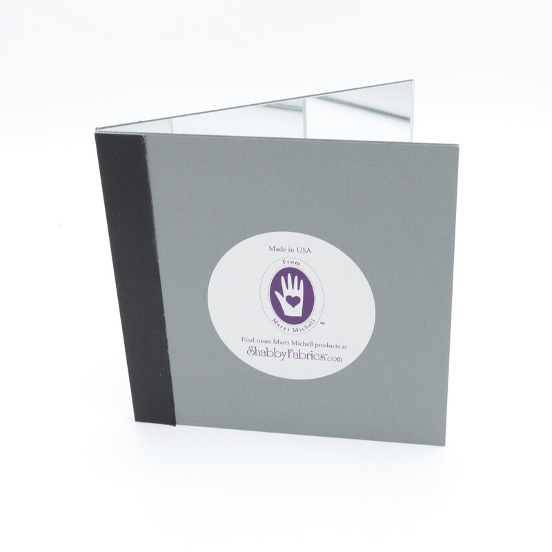 The gray Magic Mirror with a black spine, slightly opened and featuring the Marti Mitchell/Shabby Fabrics logo with a purple handprint.