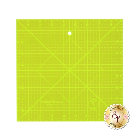 A square, bright yellow quilting ruler featuring a grid pattern with measurements and a central hole.