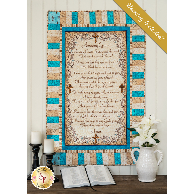 Cream, beige, and aqua colored quilt featuring a script of the Amazing Grace, hung on a cream paneled wall and staged with a bible and coordinating decor.