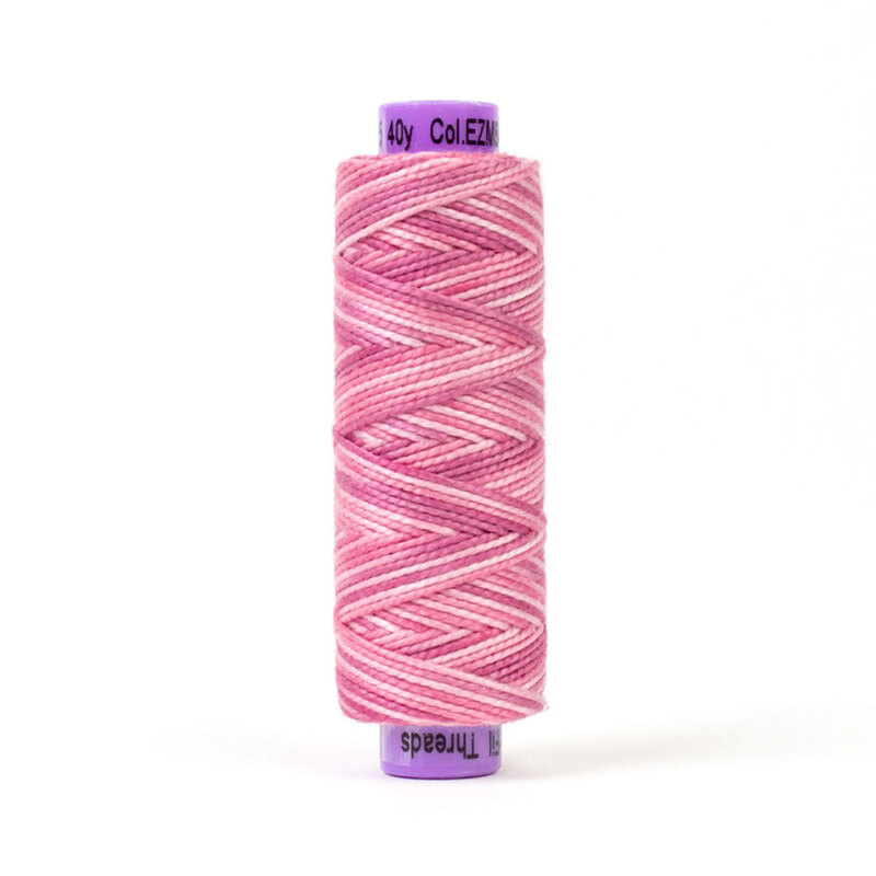 A spool of pink and white thread with a zigzag pattern, topped with a purple label.