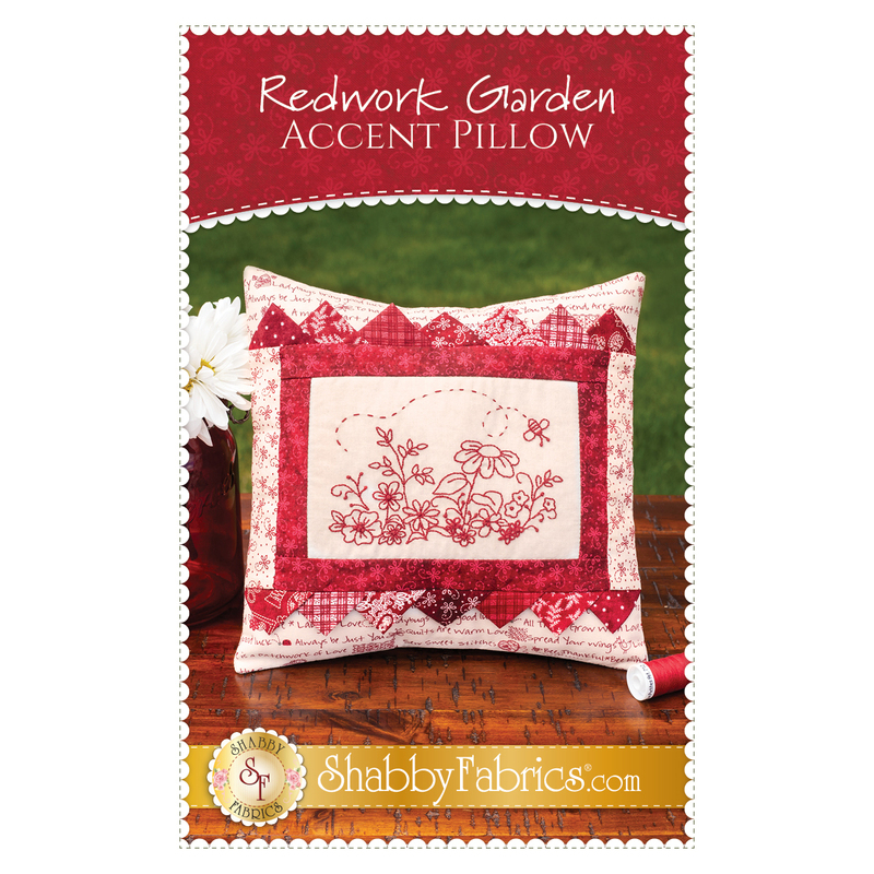 The front of the Redwork Garden Accent Pillow Pattern, showing the finished redwork pillow displayed on a wooden table with flowers peeking from the side of the frame.